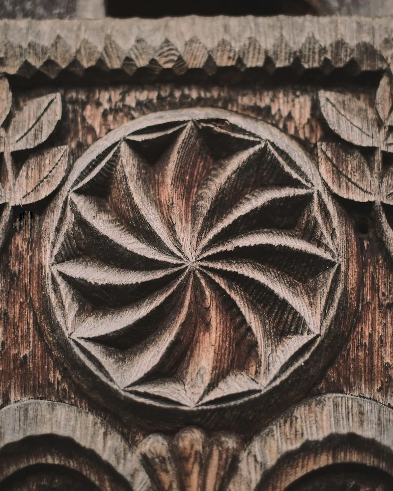 Detalle de un panel de madera con roseta tallada de pétalos radiales y cenefa dentada en el borde superior